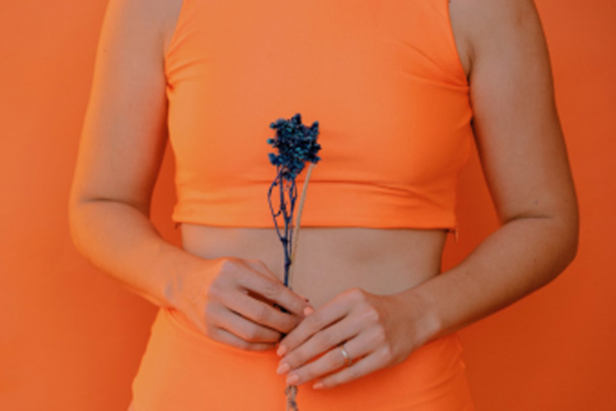An image of a woman holding a blue flower and wearing orange clothes